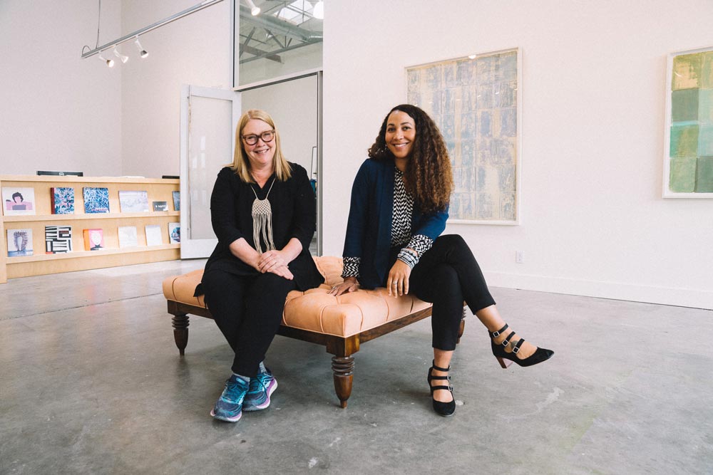 Two people sit on a large bench in an open gallery space.