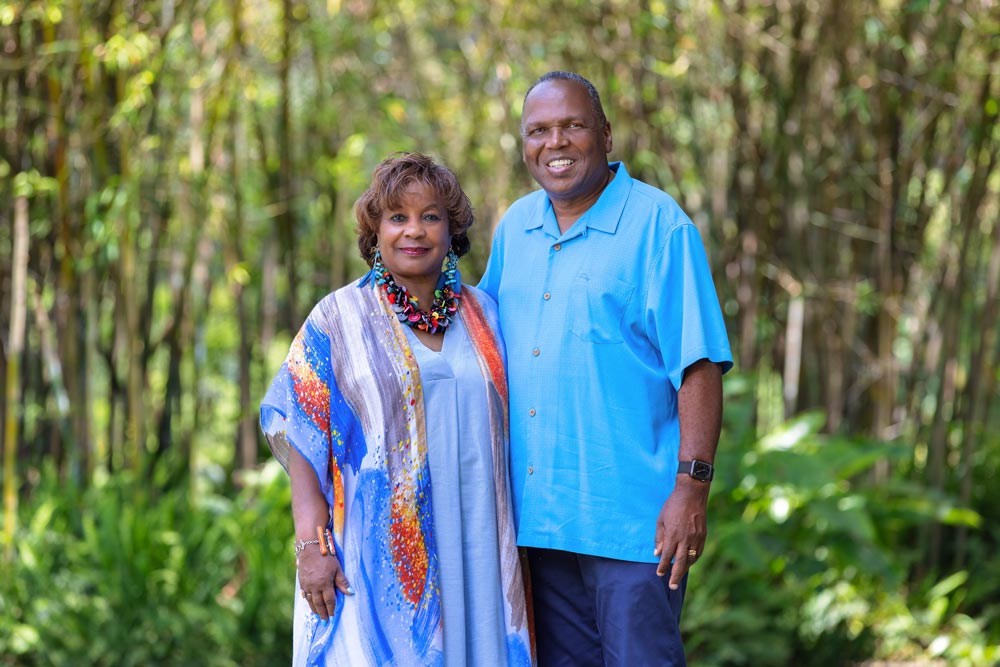 A couple dressed in blue stands among a grove of bamboo and ferns.