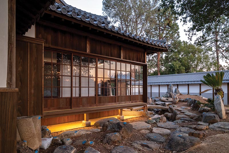 A soft light glows under a large exterior window that looks onto a rock garden.