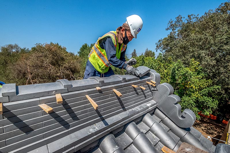 A construction worker in a hard hat lays tiles on a roof.