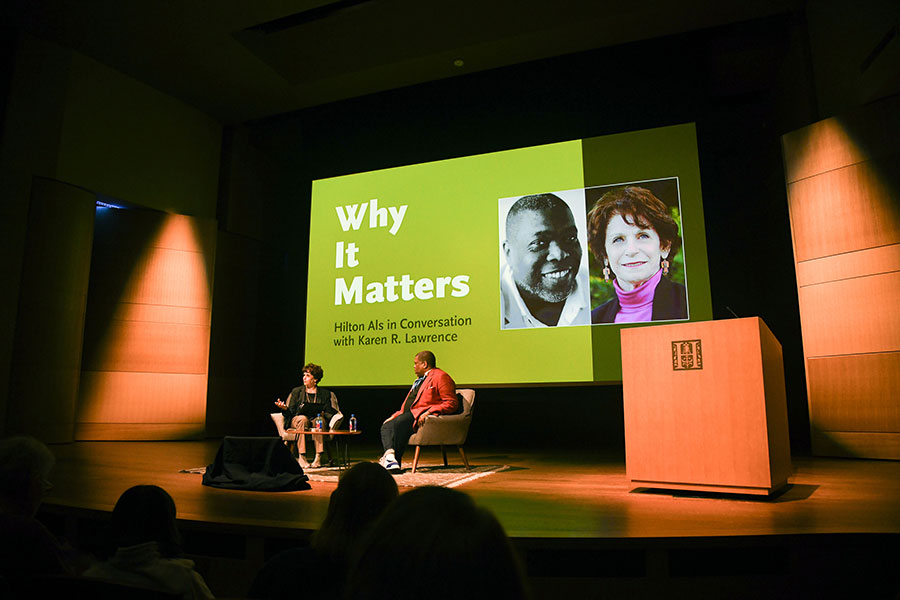 Two people on a stage in front of a projected slide with the event title.