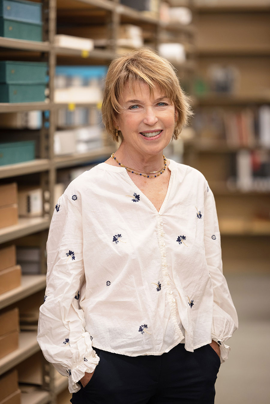 A person poses for the camera in front of shelves of books and boxes.