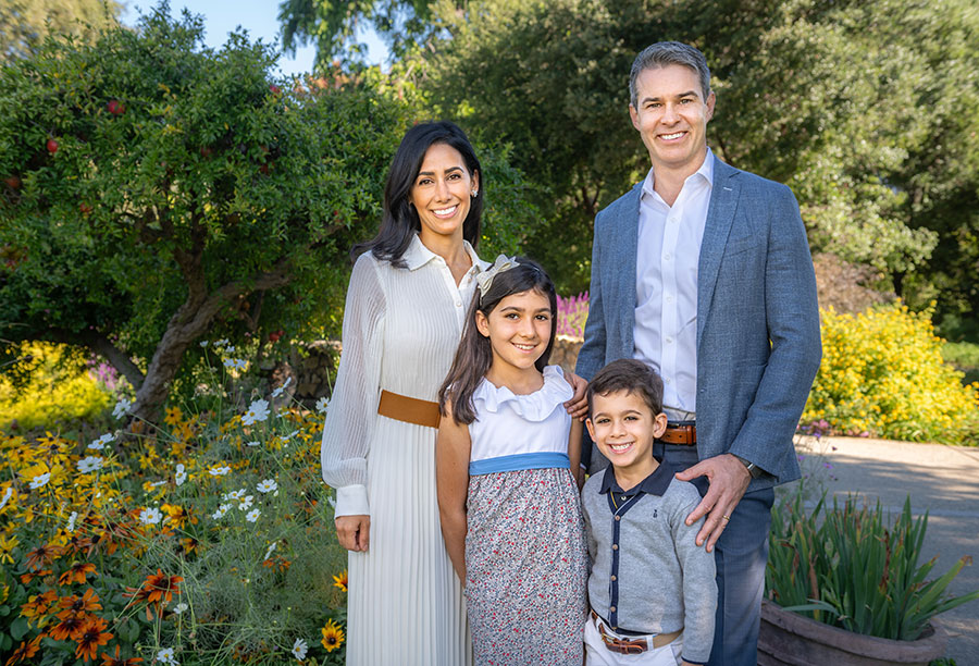 A family of four poses for the camera in a garden.