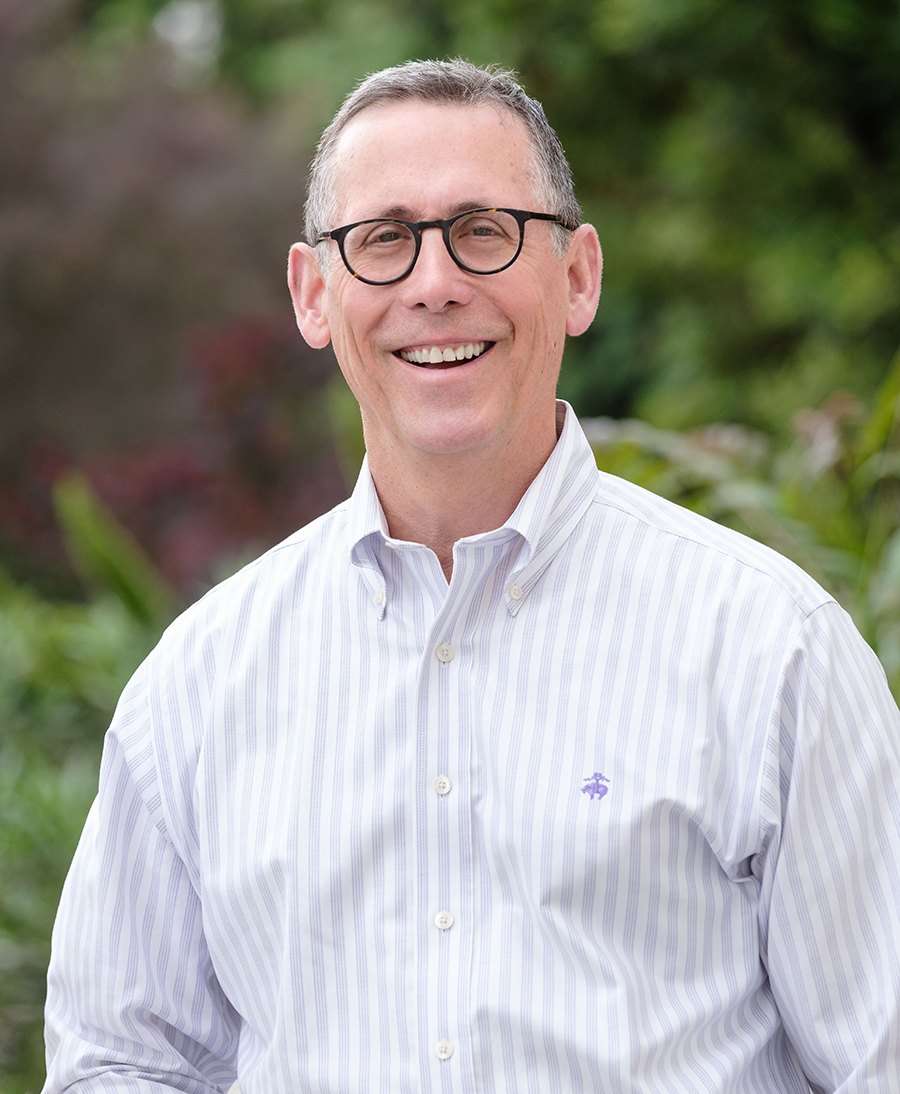 A smiling person wearing glasses and a striped shirt.