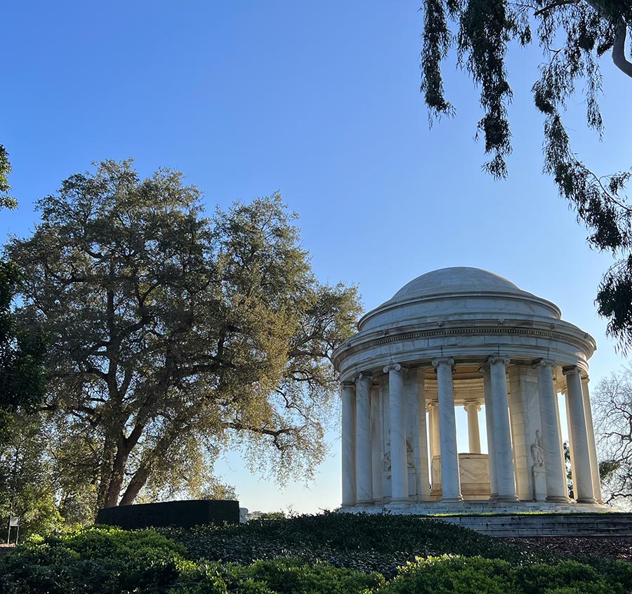 A mausoleum stands next to a large oak tree on a hill.