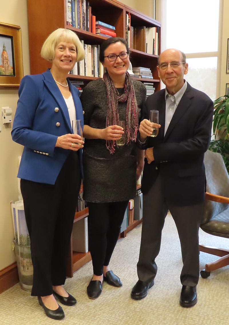 Three people stand together with drink glasses in their hands.