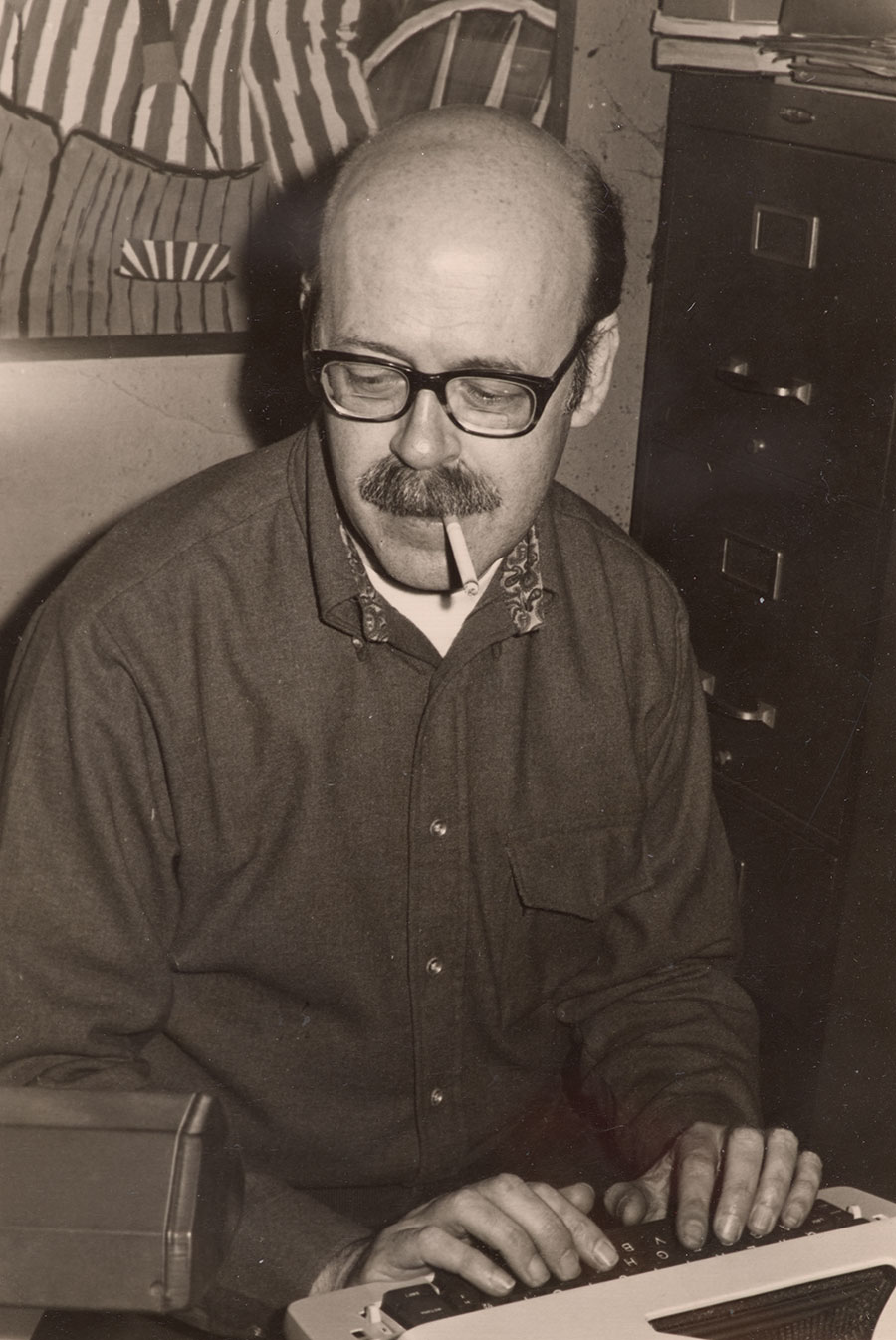 Black-and-white photo of person typing with cigarette in mouth.