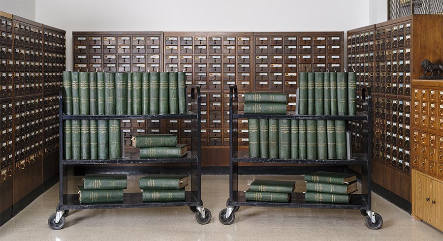 Fifty large books sit on two book carts, surrounded by card catalog drawers.