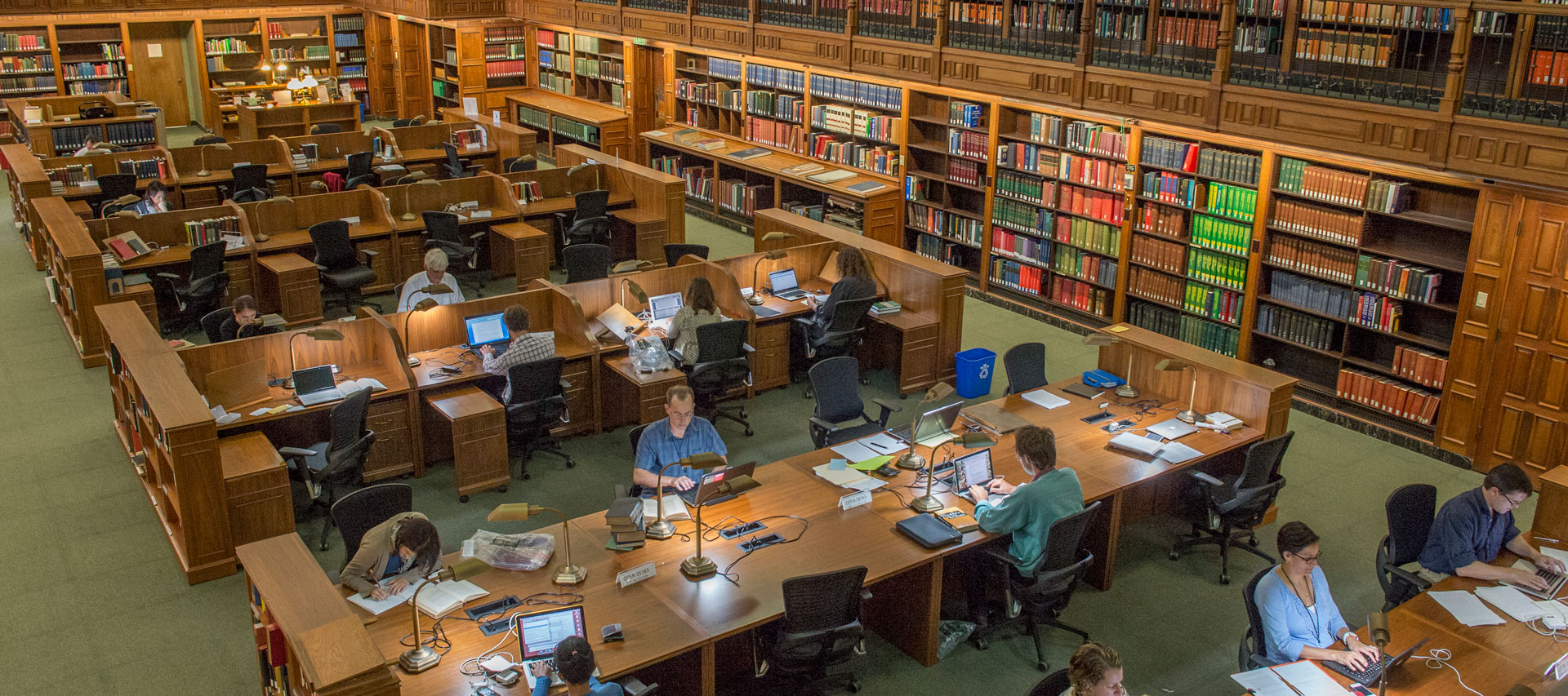 A large room with long desks for multiple people, and walls lined with bookshelves on two levels.