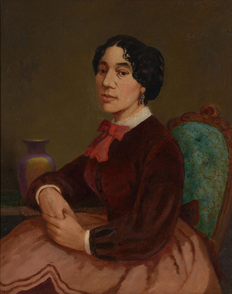 Portrait of a woman wearing a plum velvet top and red bow tie while sitting on a blue-and-gold chair.