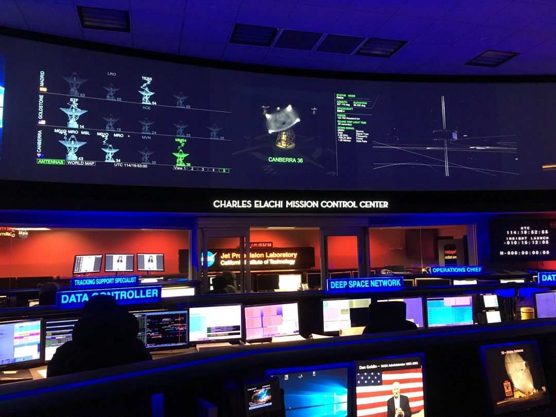 A dark room filled with computer screens and a sign that says, “Charles Elachi Mission Control Center.”