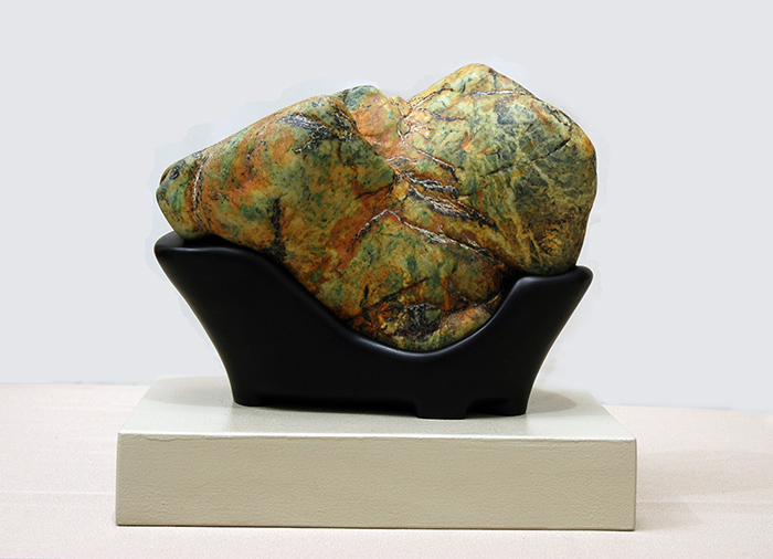 A green and orange stone in a black wooden display cradle.