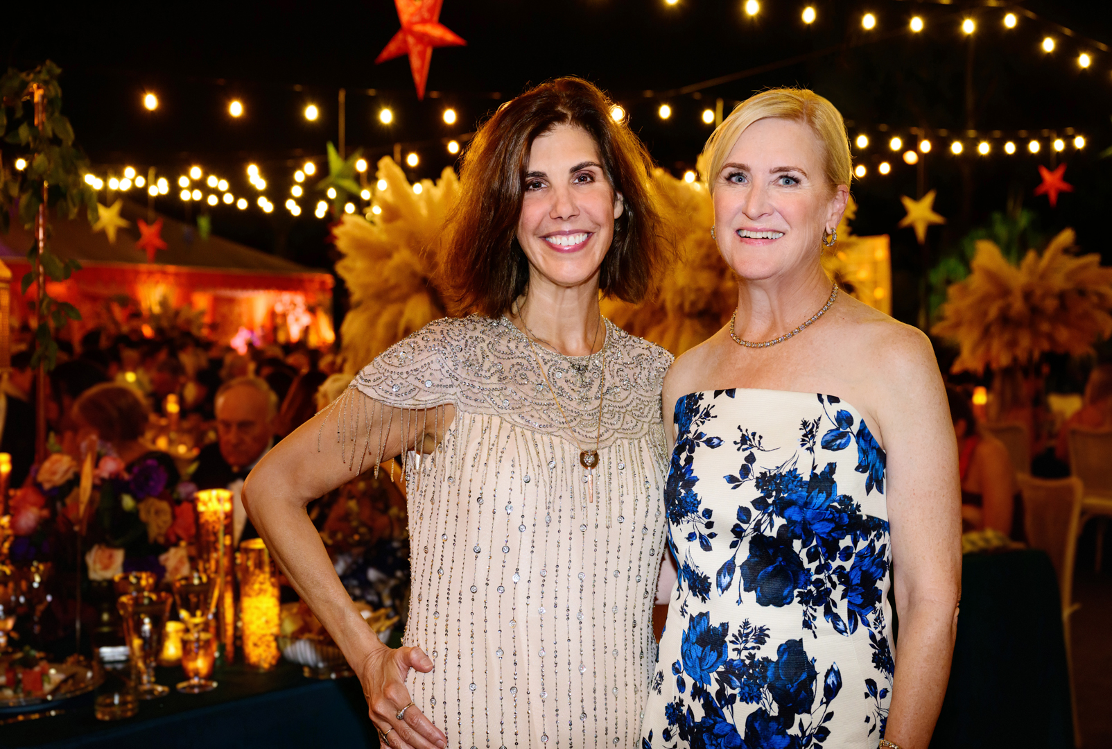 Two people pose near an outdoor party at night.