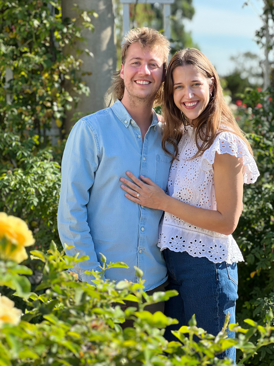 A smiling couple stands in a green garden.