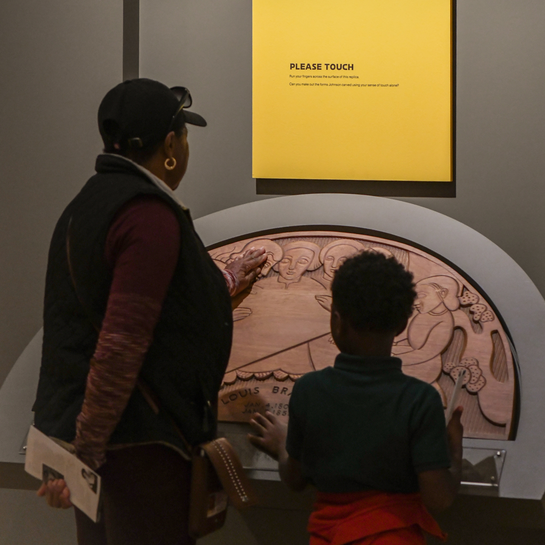 Two people touch a replica of an artwork in a gallery.