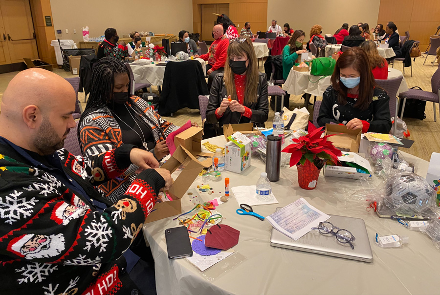 A group of adults sits at a table, working on individual art projects, in a large conference room filled with tables and participants.