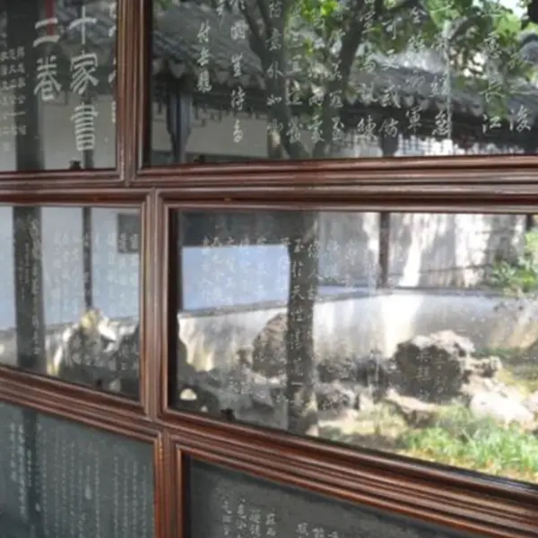 A collection of stone slabs with Chinese writing are framed in dark wood on a wall. A wall and roof are reflected on the glass that covers the slabs.