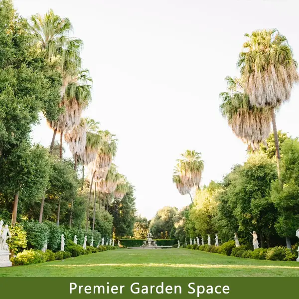 Looking down the center of a grassy vista with palm trees and statues lining both sides.