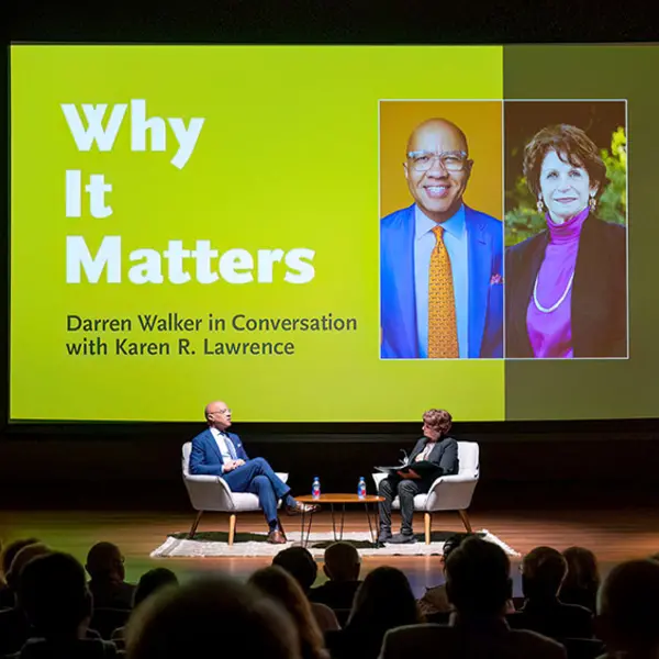 An audience watches two people have a conversation on a stage, where a large graphic says, “Why It Matters.”