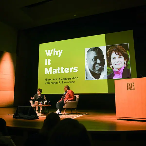 Two people on a stage in front of a projected slide with the event title.