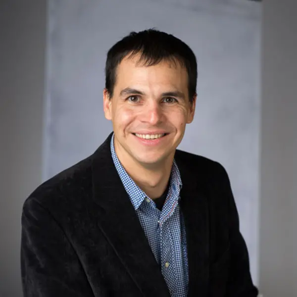 A smiling person in a blue shirt and dark suit jacket.