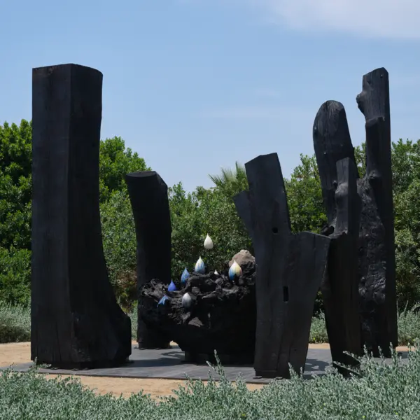 A large sculpture in a garden, created with charred wood and ceramics.