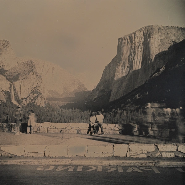 A grayscale image of people near a paved road in a national park with large mountains and a forested valley.