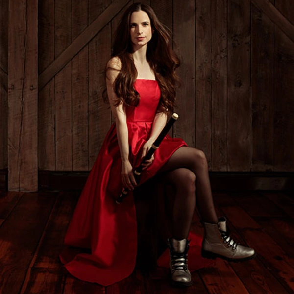 A musician in a red dress holds a flute at their side.