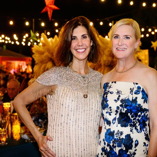 Two people pose near an outdoor party at night.