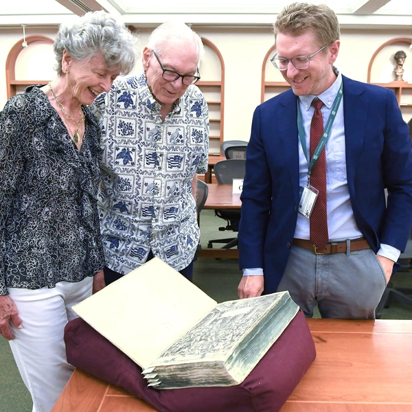 Three people look at an open book in a library.