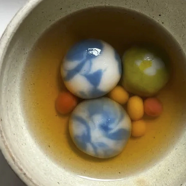 A ceramic bowl with clear-brown broth and colorful rice balls.