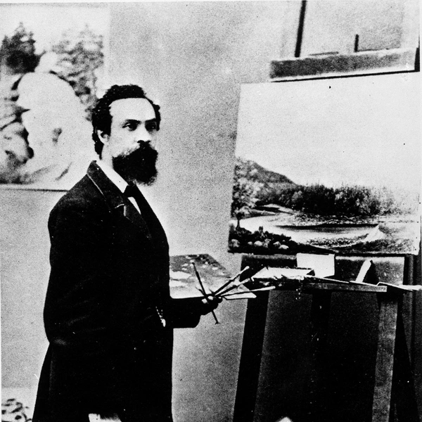 A black-and-white photo of a man in a suit, holding a palette and brushes in front of an easel.