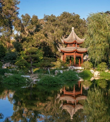 A Chinese-style garden with a tiered-tower structure surrounded by trees and shrubs, reflecting in a large body of water.