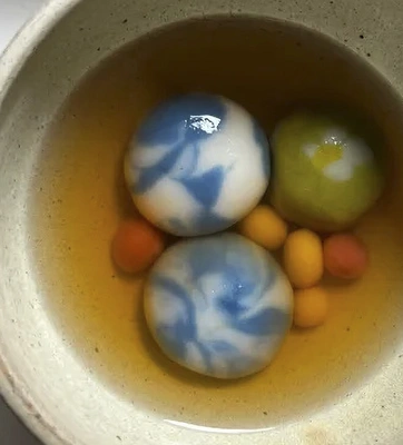 A ceramic bowl with clear-brown broth and colorful rice balls.