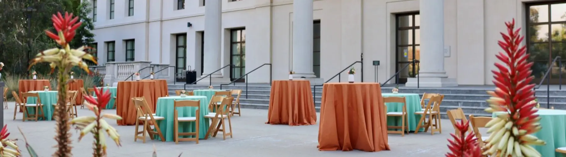 A courtyard filled with party tables covered in teal blue and darker peach tableclothes.