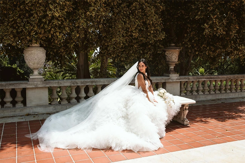 A bride in a flowing wedding gown and train looks behind her.