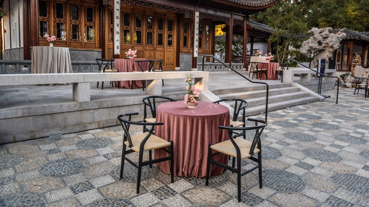 A few round tables with rose-colored tablecloths set up around a courtyard.