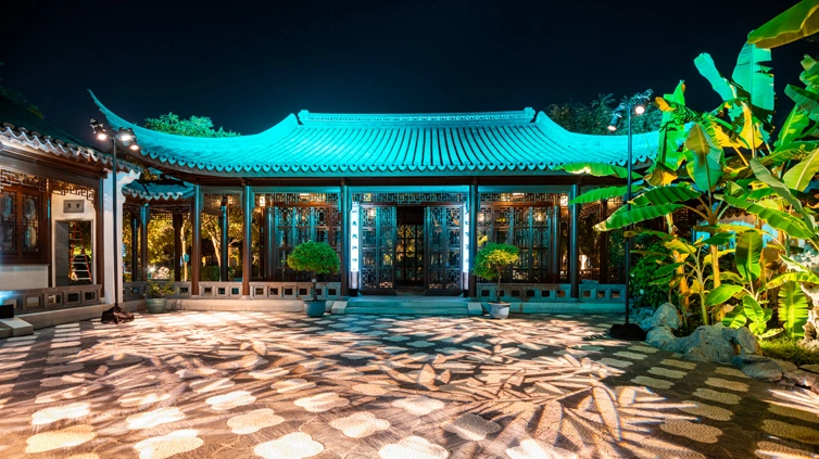 Teal blue lights shine on the roof of a Chinese-designed glass building.