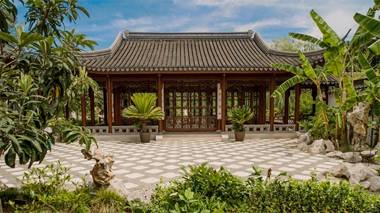 Lush green trees reveal a Chinese-influenced building with glass doors and windows.