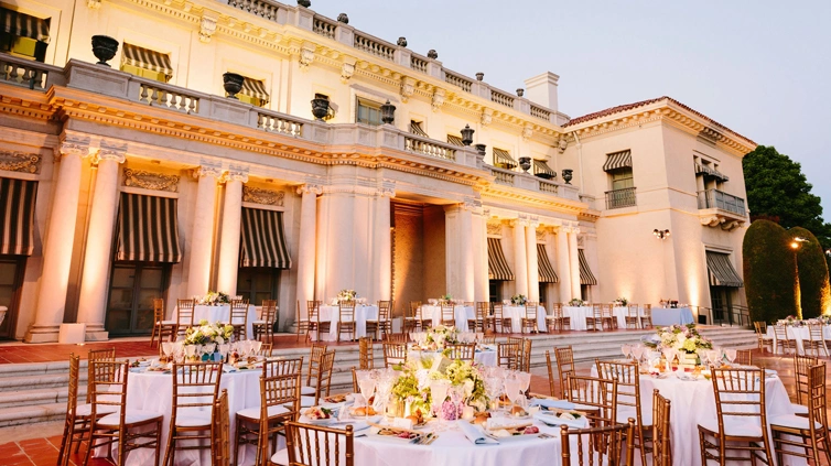 White tablecloths hang on round event tables accented by wooden chairs.