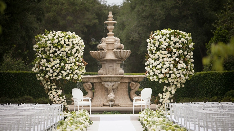 Large white rose-filled structures point towards a stage area with two white chairs angled towards each other.