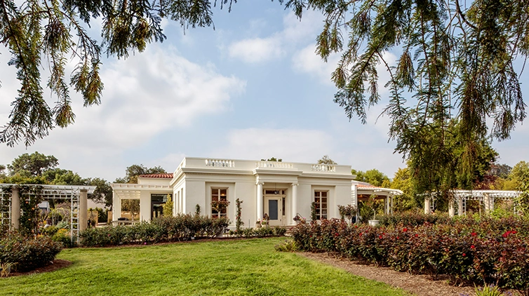 The exterior of a restored 1910s building stands among a garden.