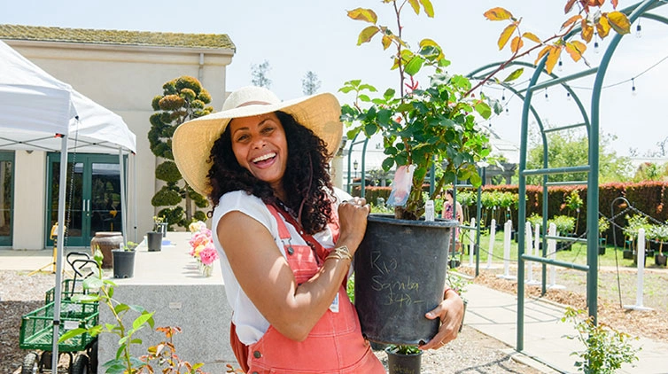 A guest holds a plant and smiles brightly for the camera.