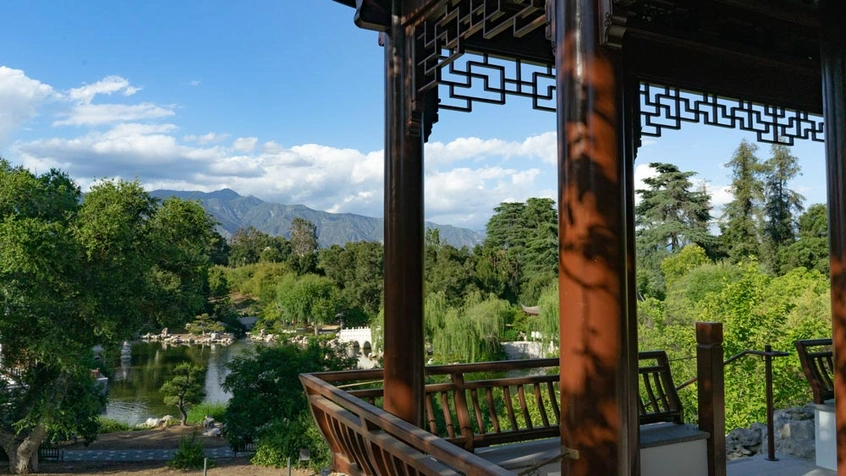 Reddish brown columns frame a panoramic view of a garden surrounding a body of water and mountains in the distance.