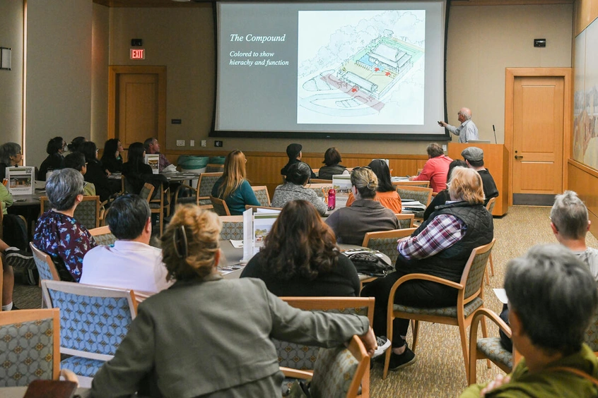 A group of people sit at tables watching a presentation.