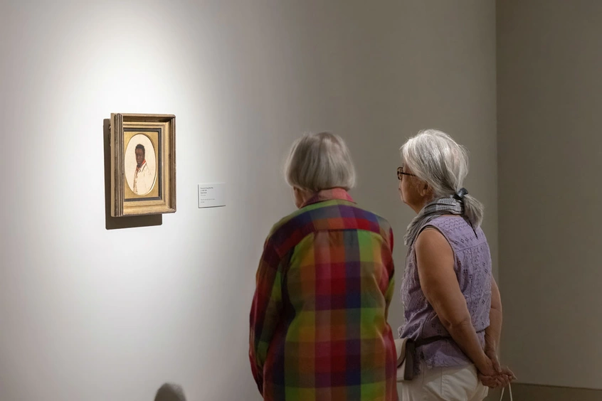 Two people stand looking at painting on a wall.