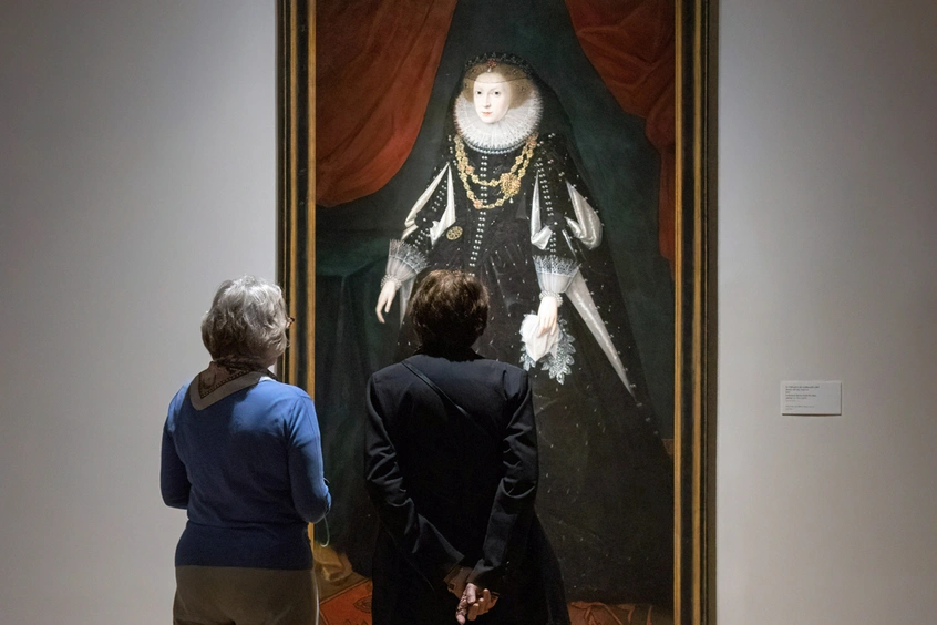 Two people stand looking at painting on a wall.