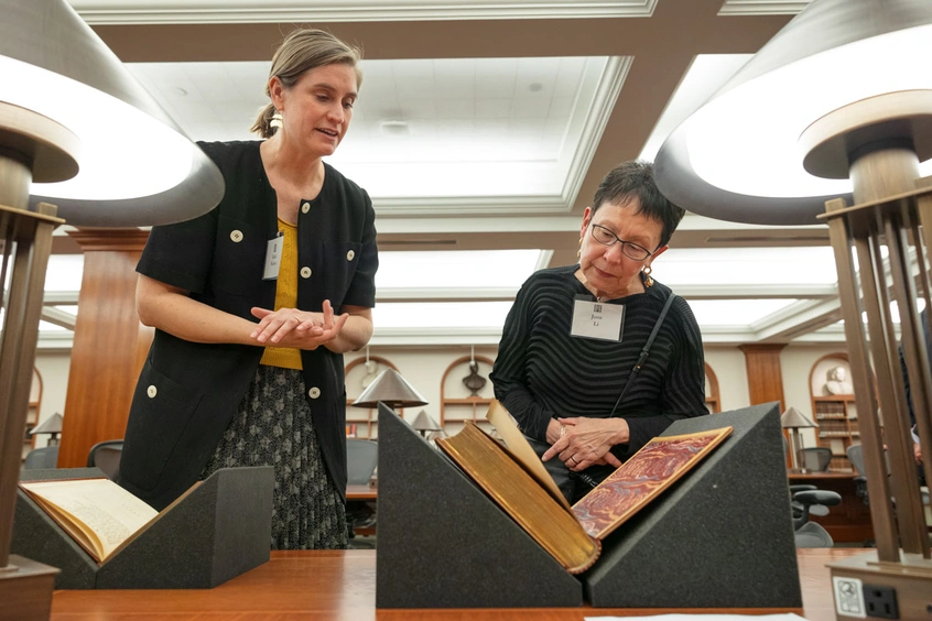 Two people stand looking at an open book.