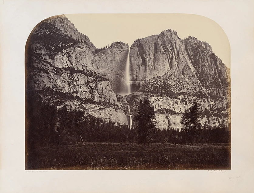 A black and white photograph of a great mountain range with a waterfall in the middle.