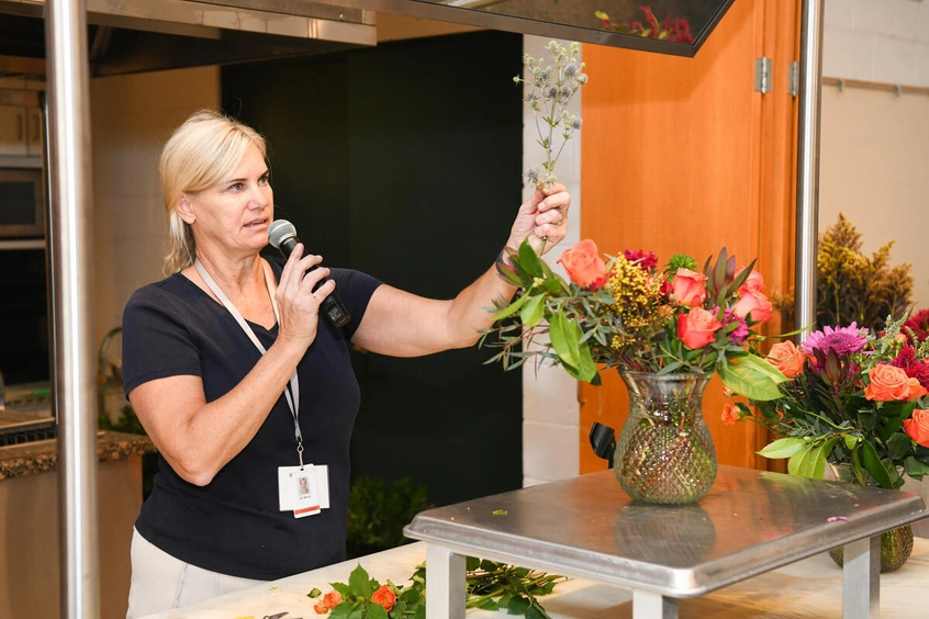 An instructor holding up baby's breath while speaking into a microphone.